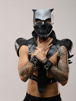 the man in a bdsm demon skull mask, dressed in a leather cloak with leather bracelets and straps on his body
