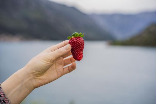 Young attractive woman eating a strawberry, outdoors.