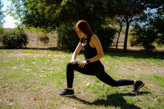 Redhead fitness woman doing lunge exercises looking at the floor concentrated for leg muscle training. Active girl doing one leg forward step lunge exercise. exercise concept