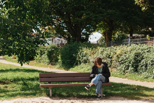 Happy girl using a smart phone in street sitting on a bench. Beautiful girl sitting on a bench, fashion life style with your phone writes a message on social networks, sunny day in the park, relaxing, after work business woman