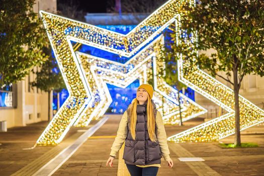 Girl walking in Christmas traditional market decorated with holiday lights in the evening. Winter portrait beautiful young woman outdoors in front of Xmas holidays decorations.