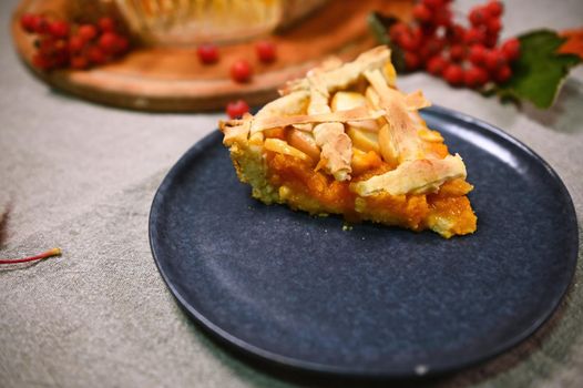 Close-up. Selective focus on a piece of a freshly baked homemade tasty American classic pumpkin pie, with crispy crust, served on a navy plate, for Thanksgiving dinner. Autumn still life with food