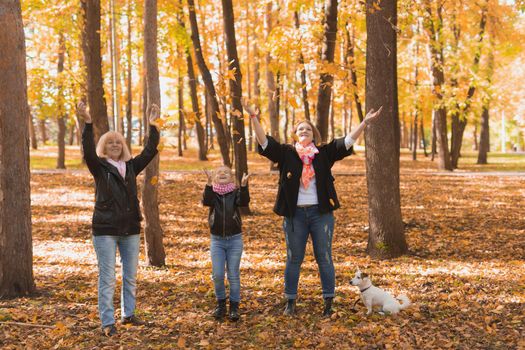 Grandmother and mother with granddaughter throw up fall leaves in autumn park and having fun. Generation, leisure and family concept