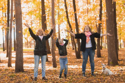 Grandmother and mother with granddaughter throw up fall leaves in autumn park and having fun. Generation, leisure and family concept