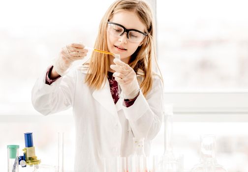 Girl doing scientific chemistry experiment wearing protection glasses and measuring liquid. Schoolgirl with test equipment on school lesson