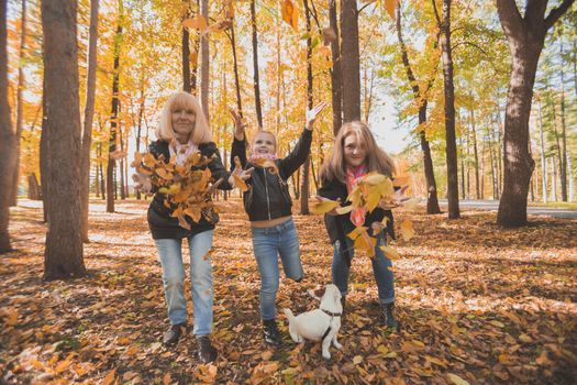 Grandmother and mother with granddaughter throw up fall leaves in autumn park and having fun. Generation, leisure and family concept