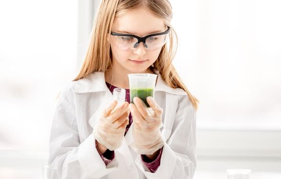 Girl doing scientific chemistry experiment wearing protection glasses. Schoolgirl with equipment and chemical liquids on school lesson