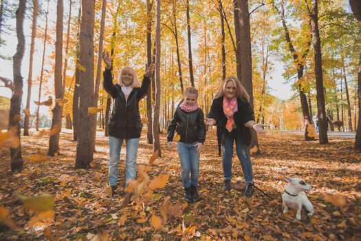 Grandmother and mother with granddaughter throw up fall leaves in autumn park and having fun. Generation, leisure and family concept