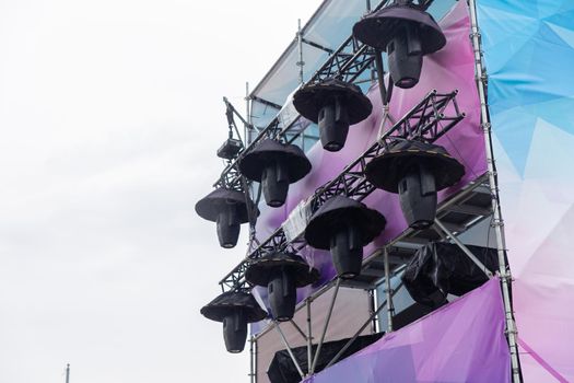 Professional lighting equipment high above an outdoor concert scene. The light sources are equipped with special umbrellas to protect against precipitation.