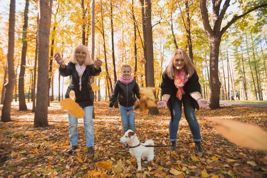 Grandmother and mother with granddaughter throw up fall leaves in autumn park and having fun. Generation, leisure and family concept