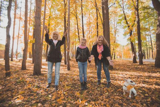 Grandmother and mother with granddaughter throw up fall leaves in autumn park and having fun. Generation, leisure and family concept