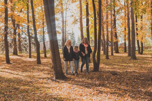 Grandmother and mother with granddaughter throw up fall leaves in autumn park and having fun. Generation, leisure and family concept