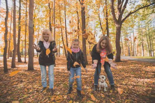 Grandmother and mother with granddaughter throw up fall leaves in autumn park and having fun. Generation, leisure and family concept