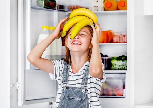 Preteen girl with bananas vitamin healthy food at kitchen. Pretty child kid enjoying yellow fruits at home