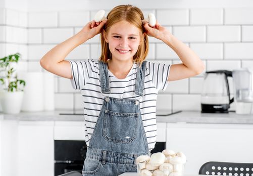 Preteen girl with champignons posing at kitchen and smiling. Pretty child with mushrooms food at home