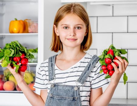 Preteen girl with red radish at kitchen posing and smiling. Pretty child with fresh vitamin vegetables at home