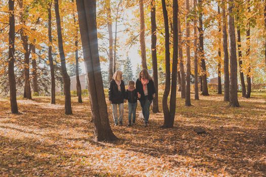 Grandmother and mother with granddaughter throw up fall leaves in autumn park and having fun. Generation, leisure and family concept