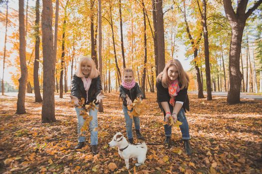 Grandmother and mother with granddaughter throw up fall leaves in autumn park and having fun. Generation, leisure and family concept