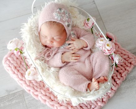 Newborn baby girl sleeping in basket decorated with flowers. Infant child kid spring blossom studio portrait