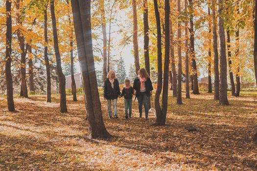 Grandmother and mother with granddaughter throw up fall leaves in autumn park and having fun. Generation, leisure and family concept