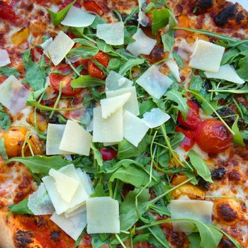 Vegetarian pizza with fresh ingredients: tomatoes, rucola salad, Parmesan cheese. Baked in a stone oven.