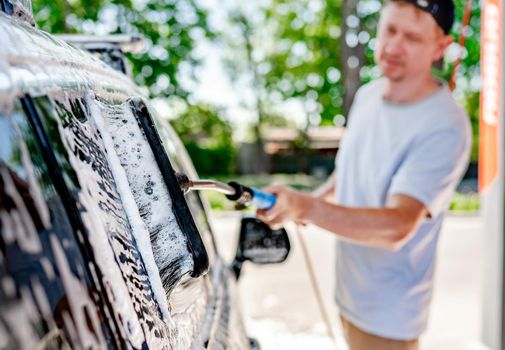 A man washing a car at a self-service car wash with a brush