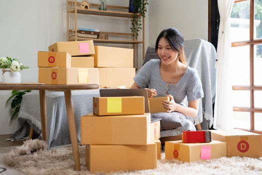 Start up small business, SME female owner checking order online to prepare to pack a box of goods for sale to customers, sme business idea.