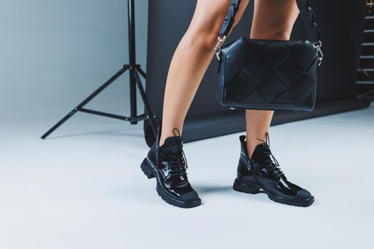 Close-up of female legs in black leather lace-up shoes. Black leather handbag in female hands. New autumn collection of women's leather shoes 2022