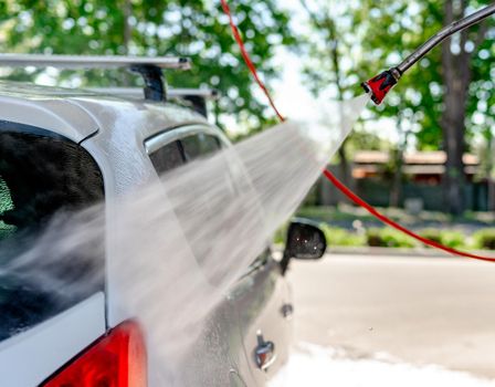 Shot of a man washing his car under high pressure water outdoors.