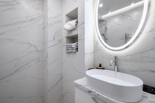 White bathroom interior with marble tiles on the walls and a round mirror