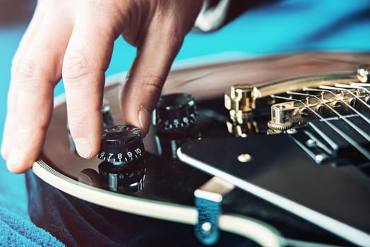 Male hand changing electric guitar settings. Tuning a timbre regulator. Close-up view