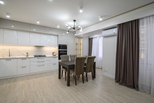 Large modern new well designed white kitchen interior after renovation in studio apartment, panoramic windows covered with curtains, plenty of copy space