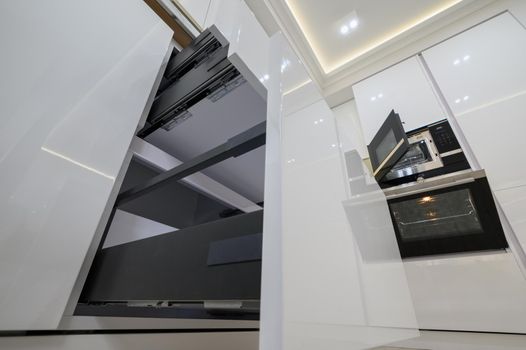 White modern kitchen with a stove, oven and microwave with open doors, drawers pulled out, high angle view