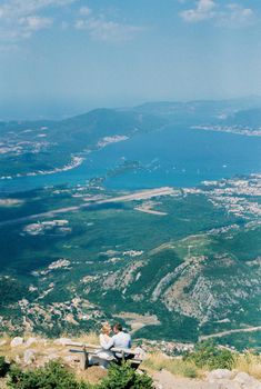Bride and groom are sitting on a bench on a mountain above the Kotor Bay. High quality photo