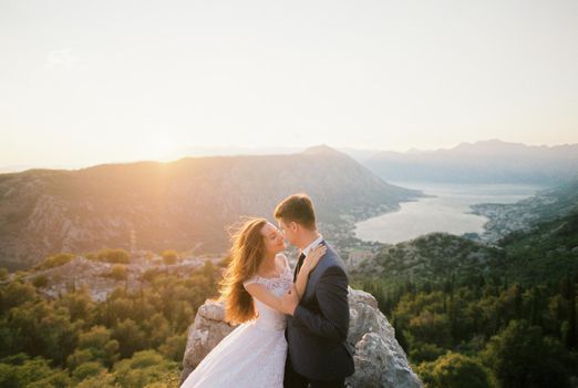 Groom hugs bride standing on the top of the mountain above the valley. Kotor, Montenegro. High quality photo