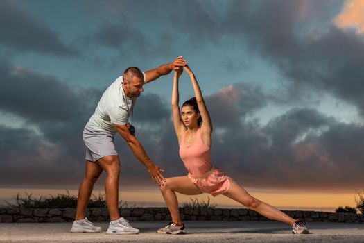 Man fitness trainer trains girl outdoors near the sea