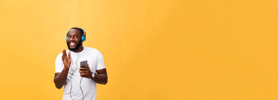 African American man with headphones listen and dance with music. Isolated on yellow background.