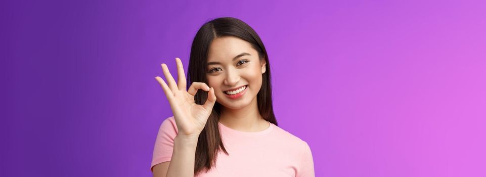 Cute smiling asian girl approve good plan, show okay ok sign, tilt head lovely grinning, satisfied perfect quality product, give positive feedback, accept choice, stand purple background.