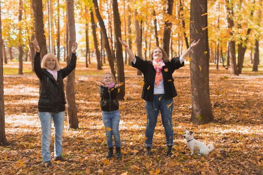 Grandmother and mother with granddaughter throw up fall leaves in autumn park and having fun. Generation, leisure and family concept