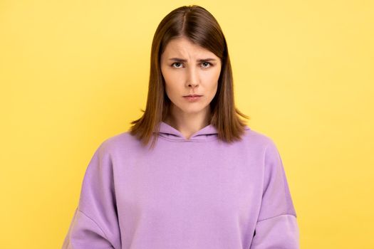 Portrait of disappointed woman being upset of bad news, looking at camera with frowning face, expressing sadness, wearing purple hoodie. Indoor studio shot isolated on yellow background.