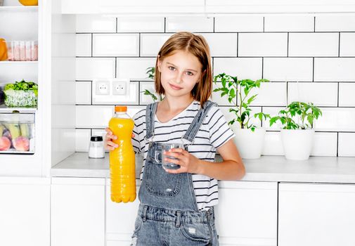 Preteen girl with orange juice bottle and glass at kitchen. Pretty child kid with vitamin fruit drink at home