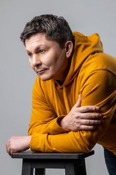 Portrait of handsome middle aged man looking pensive thoughtful, leaning on chair and looking away, being deep in thoughts, wearing urban style hoodie. Indoor studio shot isolated on gray background.