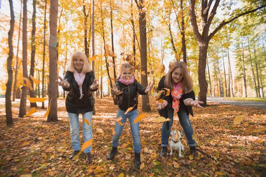 Grandmother and mother with granddaughter throw up fall leaves in autumn park and having fun. Generation, leisure and family concept