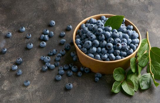 Freshly picked blueberries in a bowl. Juicy and fresh blueberries with green leaves on a rustic table. Blueberries on a wooden background. Blueberries antioxidant.