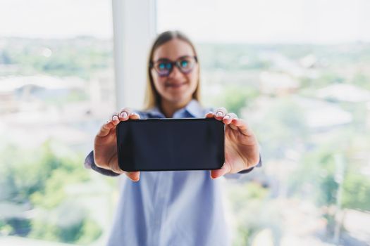 A modern mobile phone with a black screen is held in the hands of a woman, female hands with a smartphone close-up