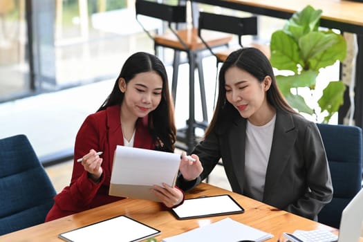 Two businesswoman analyzing financial reports together at modern workplace.