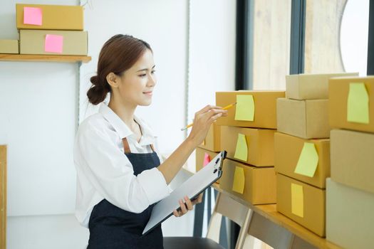 Asian female small online business owner packing boxes on table and checking retail order preparing for shipment. Online business, e-commerce concept.