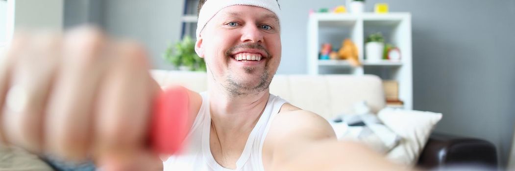 Young man doing exercises with dumbbells smiling at camera. Home fitness and sport concept