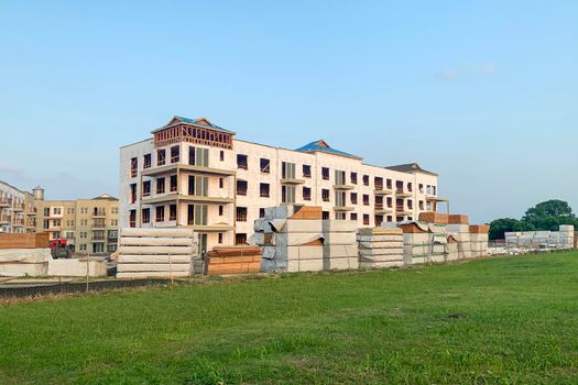 Outdoor shot of modern apartment buildings in a green residential area, house under construction surrounded by a large amount of lumber.