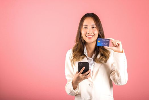 Happy Asian portrait beautiful cute young woman excited smiling hold mobile phone and plastic debit credit bank card, studio shot isolated on pink background, female using smartphone online shopping